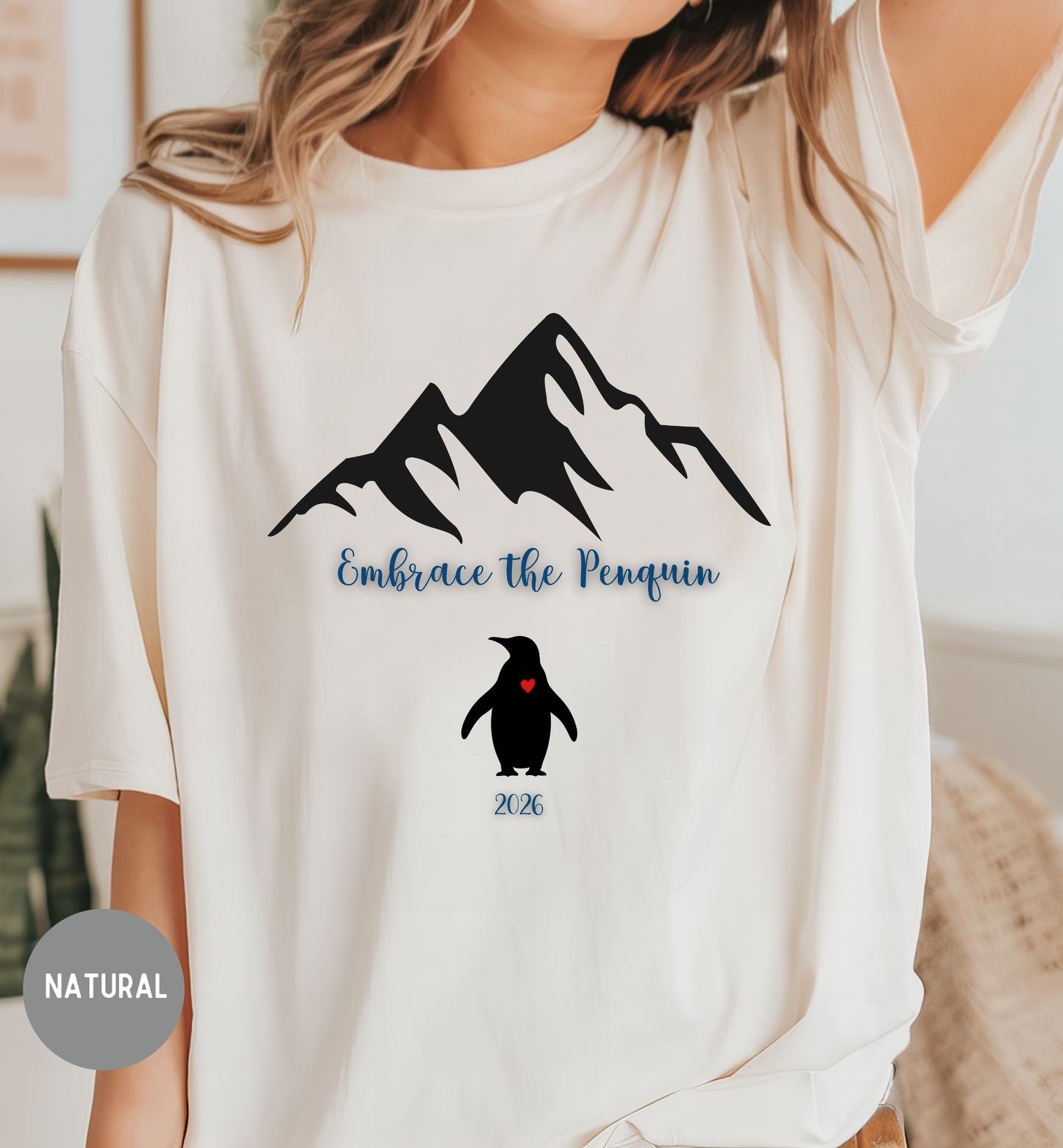 White t-shirt with mountain and penguin design, text 'Embrace the Penquin 2026', worn by a person.