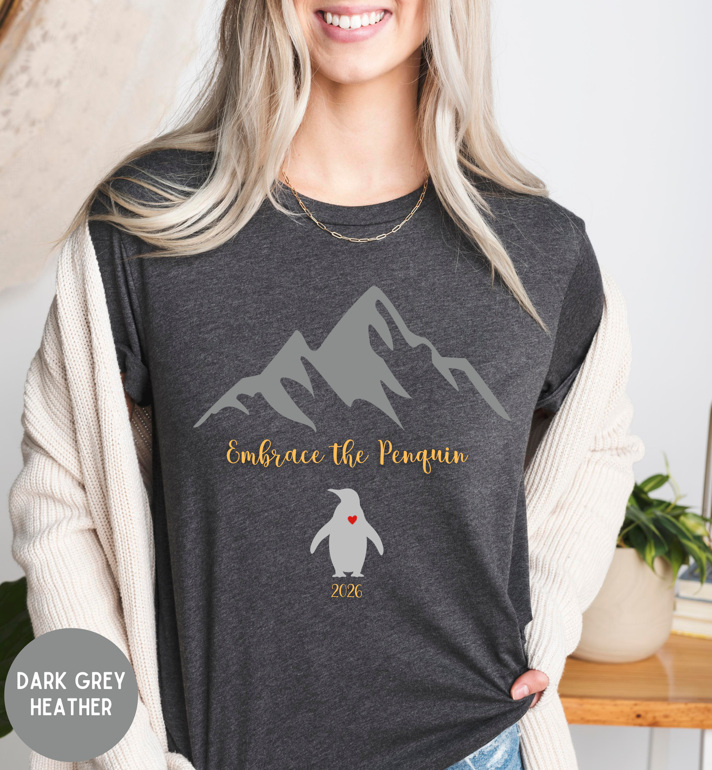Person wearing a dark grey heather t-shirt with mountain and penguin design, standing indoors.