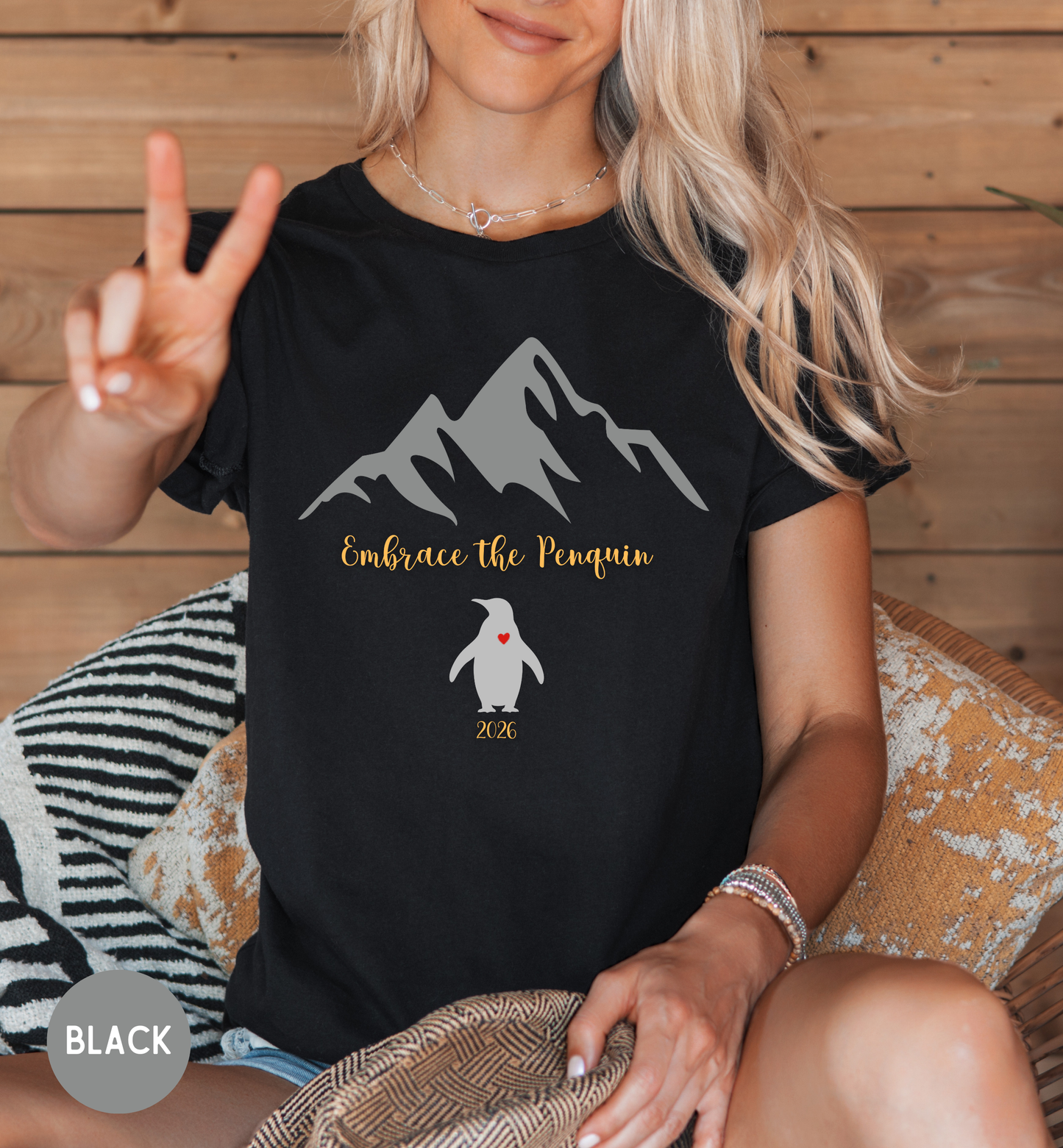 Person wearing a black t-shirt with a penguin graphic and text, sitting on a wooden floor.